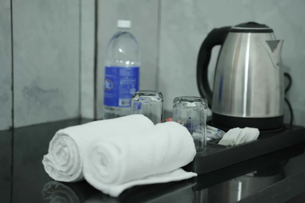 Room amenities at Gold Suite Kakkanad including electric kettle, drinking water bottle, and fresh towels for guests staying in rooms in Kakkanad.