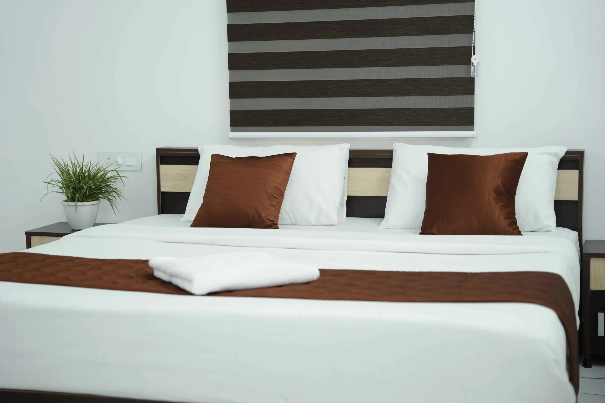 Modern, well-furnished hotel room at Gold Suite featuring a comfortable double bed, clean white linens, and elegant brown accents — best hotel rooms in Kakkanad near Infopark.